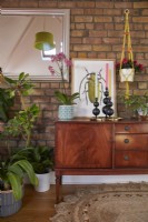 Attic living room detail with a mid century sideboard with plants, candles and artwork against an exposed brick wall.