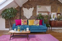 Attic living room with a teal blue sofa, mid century furniture and a macrame hanging on exposed brick.