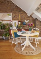 Attic living room with white round table and chairs. Mid century furniture, plants and exposed brickwork in the background.