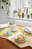 Detail of croissants and teapot on the drop leaf dining table. With cacti on the window ledge in the background.