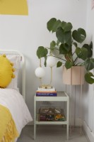 Bedroom detail showing bedside table with table lamp and a plant. 