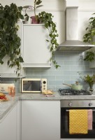 Kitchen with blue metro tiles, hanging plants, a microwave and a green saucepan.