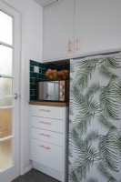 Kitchen detail showing fridge covered in jungle vinyl, microwave and a fruit basket.
