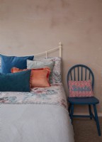 Bedroom detail showing plastered walls, a wrought iron bed with colourful printed bedding.