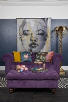 Living room with dark blue walls, a purple sofa and large illustrated poster of a woman.