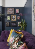 Living room detail showing dark blue walls with artwork and a purple sofa with printed cushions.