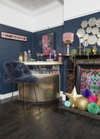 Living room with a gold drinks bar, dark blue painted walls and a decorated fireplace.