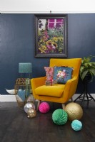 Living room with dark blue painted wall, a mid century style yellow chair, artwork and Christmas decorations.