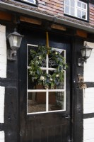 Christmas wreath on a black and white country cottage front door with vintage outdoor wall lights