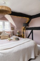 Country style attic bedroom with pink walls and exposed black beams