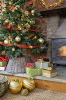 Detail of presents and baubles under a Christmas tree by a log burning stove