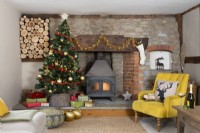 Country house living room with Christmas tree and wood burning stove and log store in a stone and brick inglenook fireplace 
