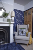 Living room with a fireplace, cosy armchair and blue patterned wallpaper.