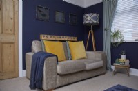 Living room with dark blue painted walls, a grey velvet sofa and a patterned floor lamp.