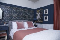 Bedroom with patterned wallpaper and dark blue walls and panelling.