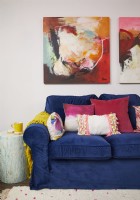 Colourful living room detail with a dark blue velvet sofa, colourful cushions and large abstract paintings.