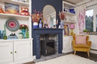 Living room with a fireplace, wood burner, alcove storage and colourful ornaments and accessories.