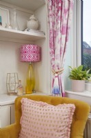 Living room detail showing yellow armchair with table lamp and pink curtains.