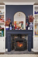 Living room with a fireplace, wood burner, alcove storage and colourful ornaments and accessories.