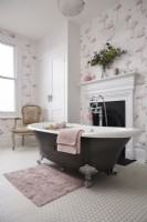 Bathroom with a rolltop bath, fireplace and flamingo wallpaper.