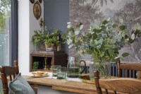 Dining area detail showing table with glassware, vintage wooden furniture, and botanical artwork.