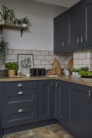 Kitchen detail showing dark grey cabinets, off white metro tiles and plants.