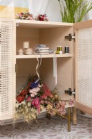 Freestanding wood craft cupboard with rattan doors storing ribbons and dried flowers 