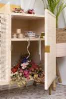 Freestanding wood craft cupboard with rattan doors storing ribbons and dried flowers 
