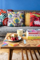 Detail of a wooden coffee table in front of a grey sofa with colourful cushions in a blue living room