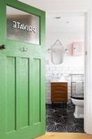 Reclaimed green door opening in to a bathroom with mid century cabinet of drawers converted to a vanity unit with sink