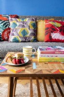 Detail of a wooden coffee table in front of a grey sofa with colourful cushions in a blue living room


