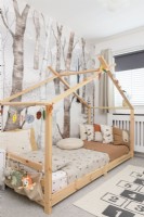 Wooden house bed in a child's bedroom in front of tree patterned wallpaper