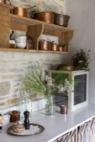 Shelf of copper pots on wall mounted shelves in country kitchen