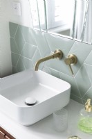 Detail of small white sink with gold taps and pale grey tiling 