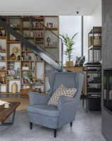A cozy space with an armchair in the background of a bookcase with decorations and stairs
