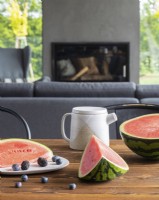 Watermelon, blackberries and blueberries lying next to a jug, and a fireplace in the background