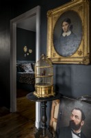 Classic portraits and golden birdcage against black painted wall