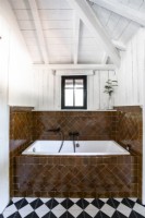 Bronze coloured tiling around bath in country bathroom