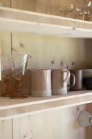 Detail of glassware and mugs on wooden kitchen shelf