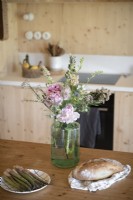 Detail of food on wooden table next to vase of wild flowers