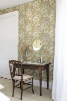 Wooden desk and chair in country bedroom with floral wallpaper
