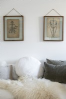 Framed paintings above sofa covered in cushions - detail