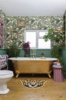 Gold bathtub in a green panelled bathroom with patterned jungle leaf wallpaper