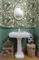 White Victorian sink in a green panelled bathroom with patterned jungle leaf wallpaper