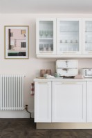 White kitchen units and reeded glass fronted cupboards in a pale pink kitchen