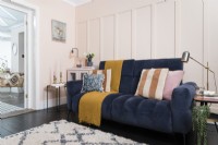 Dark blue sofa in a pale pink living room with feature panelling and conservatory beyond
