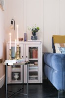 Recycled painted glass fronted cabinet in the corner of a pale pink panelled living room next to a blue sofa