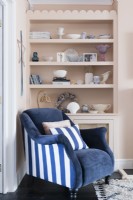 Blue and white armchair in front of scalloped shelving in the corner of a pale pink living room
