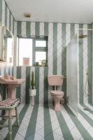 Green and white stripey tiled bathroom with pink sanitary ware