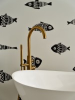 Bath tub detail with golden faucet and fish patterned wallpaper